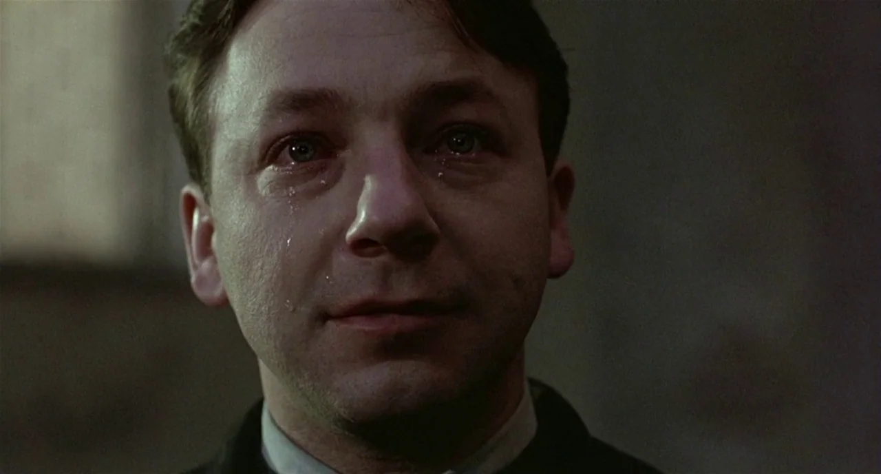 Three Colours: White (1994) movie still: closeup — A dimly lit room with muted neutral walls serves as the backdrop. A man faces the camera directly…