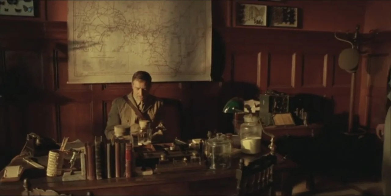 Exorcist: The Beginning (2004) movie still: medium — A wood-paneled office features a large wall map and a cluttered wooden desk. A man in uniform…