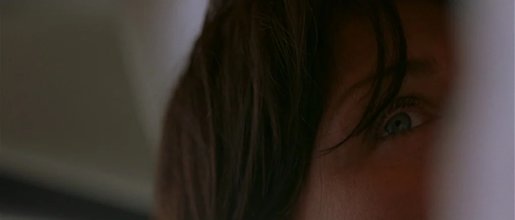 Sexy Beast (2000) movie still: closeup — A close view shows one eye peeking out from behind a dark wall partition. The subject is partially hidden…