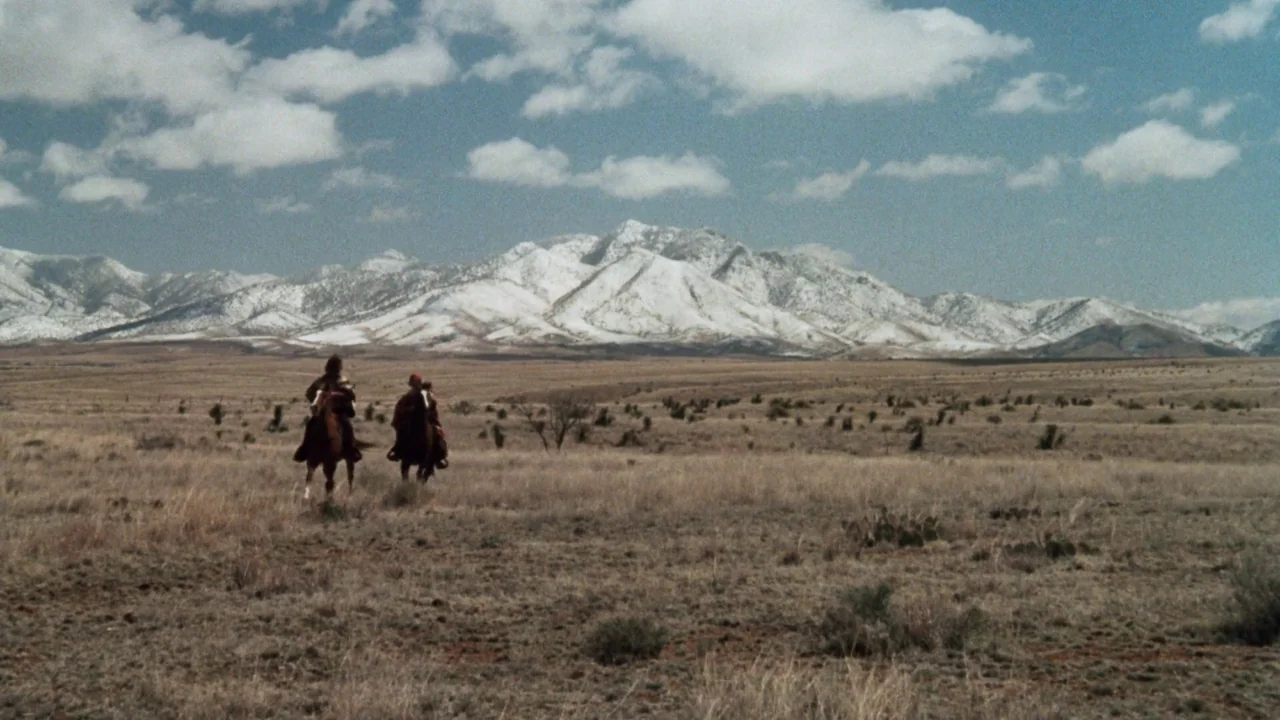 A Star Is Born (1976) movie still: wide — A vast, dry, grass-covered plain extends toward a large, snow-capped mountain range. Two individuals on…