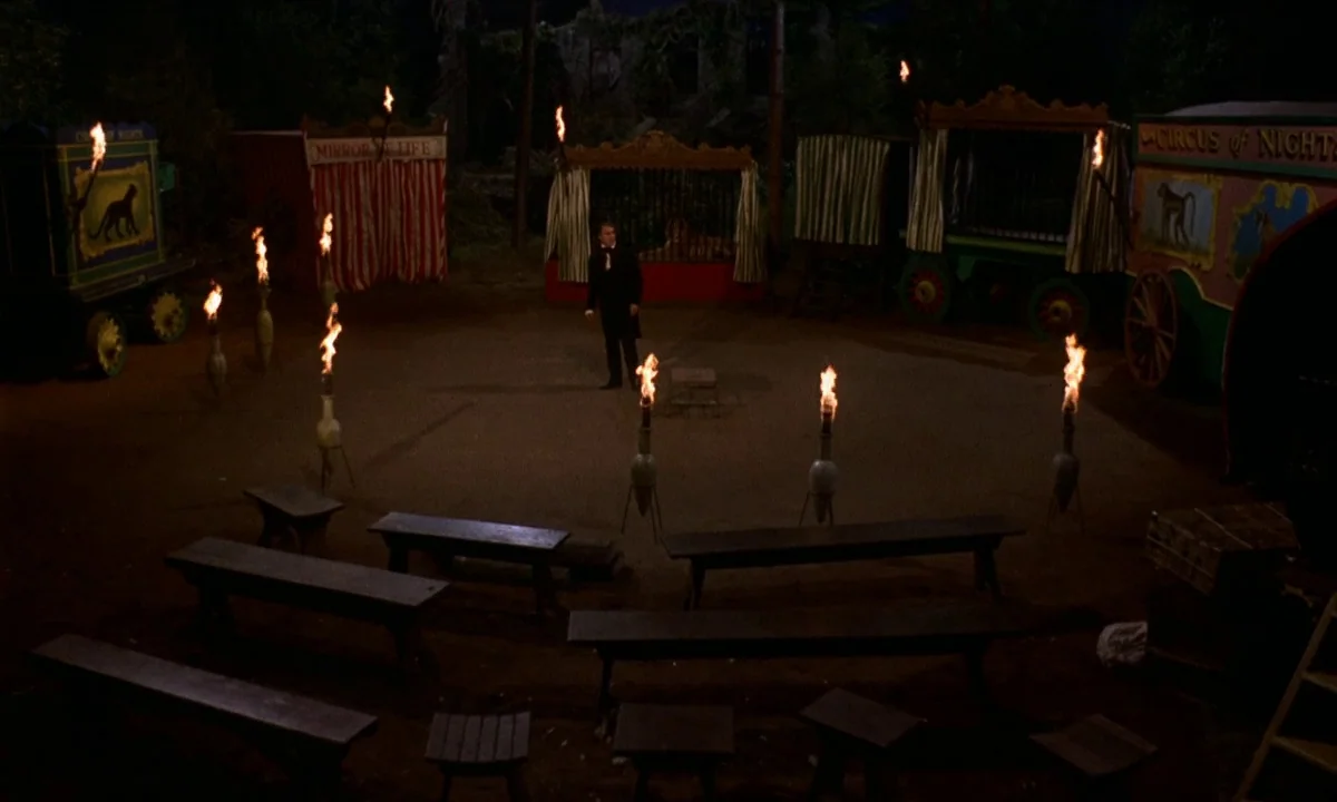 Vampire Circus (1972) movie still: wide — A nighttime fairground features a ring of burning torches encircling a central open area. A solitary man…