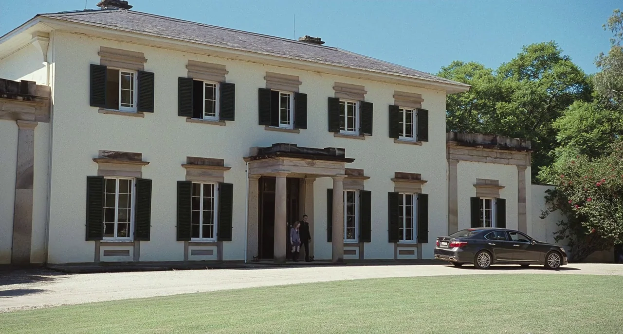 Sleeping Beauty (2011) movie still: wide — A large, two-story cream-colored mansion features symmetrical windows with dark green shutters. A modern…
