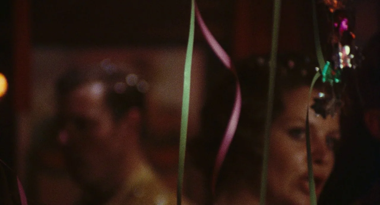 The Damned (1969) movie still: closeup — A dimly lit indoor festive space features decorative paper streamers hanging in the foreground. Two…
