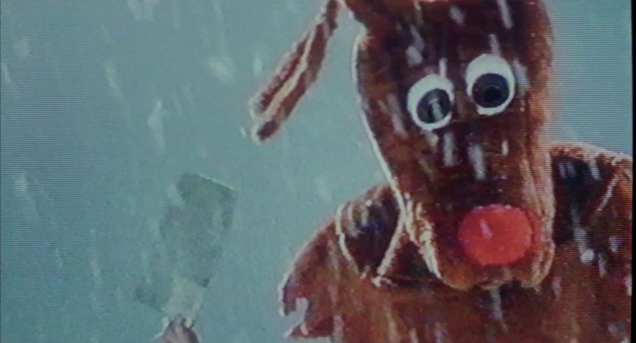 Hardware (1990) movie still: closeup — A brown reindeer puppet stands against a light blue backdrop representing a snowy environment. The character…