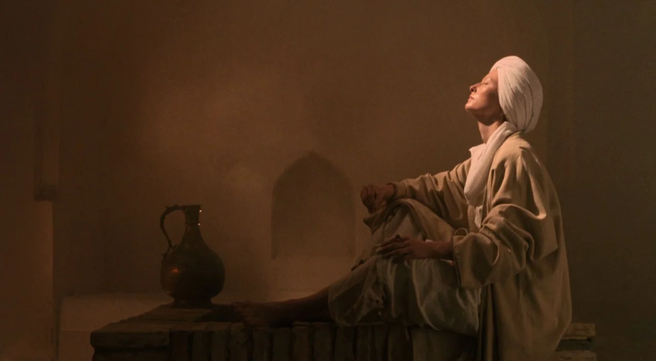 Orlando (1992) movie still: medium — A dimly lit stone room features a recessed wall niche and an ornate metal pitcher. A person in a white turban…