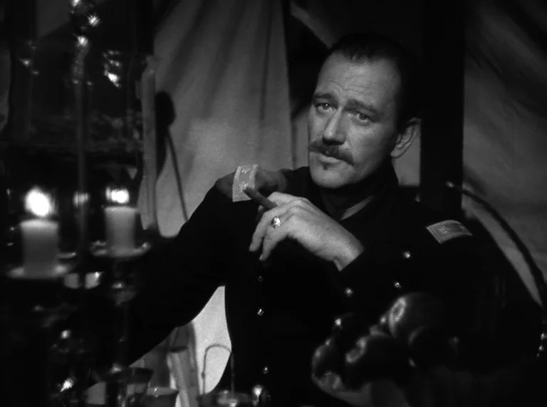 Rio Grande (1950) movie still: medium — A dark, cramped interior of a military tent with fabric walls in the background. A man in a dark uniform…