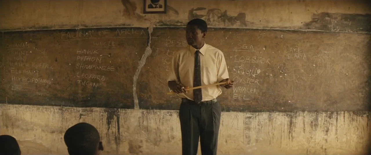 Beasts of No Nation (2015) movie still: medium — A dimly lit classroom features a worn, scratched chalkboard covered in handwritten lists of fauna.…