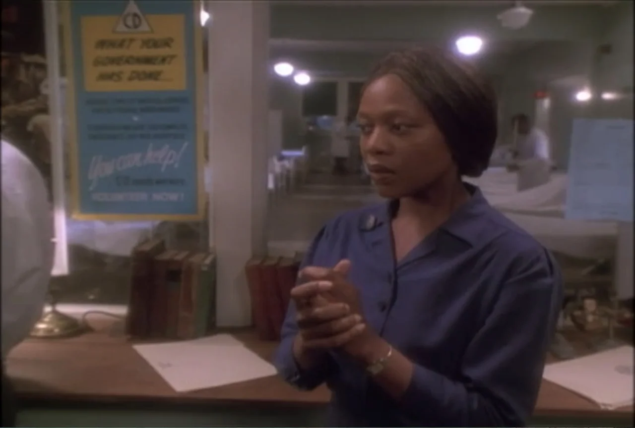 Miss Evers' Boys (1997) movie still: medium — A hospital front desk in the 1950s features a bulletin board and stack of books. A woman in a blue…