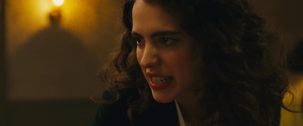 Sanctuary (2023) movie still: closeup — A dimly lit room provides a background for a close portrait of a woman. She turns her head and grits her…