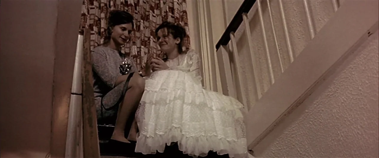 Breaking the Waves (1996) movie still: medium — A staircase with white wooden balustrades and patterned curtains visible in the background. Two…