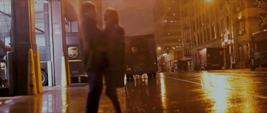 We Need To Talk About Kevin (2011) movie still: medium — A dark urban loading bay area sits adjacent to a wet city street at night. Two blurry…