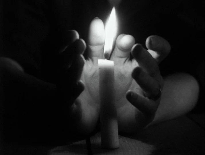 Hour of the Wolf (1968) movie still: closeup — Two hands are cupped closely around a single burning candle in a dark space. The candle flame casts…