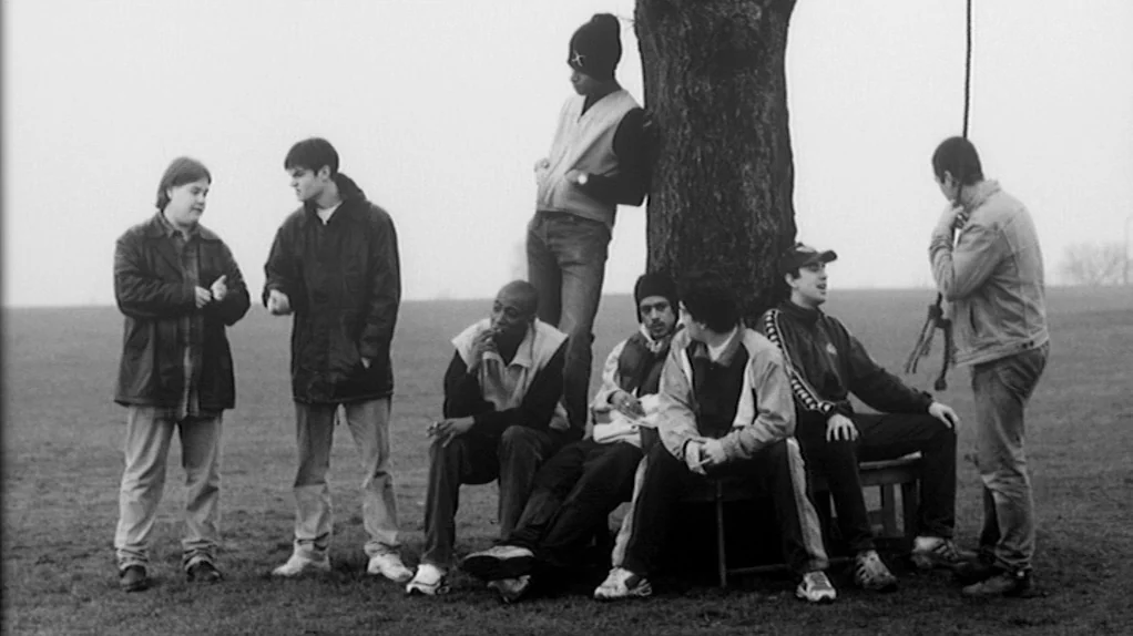 TwentyFourSeven (1997) movie still: wide — A group of young men congregate in a vast, desolate field under an overcast sky. They stand and sit…