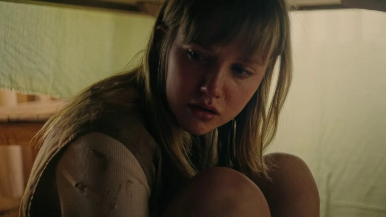 My First Summer (2020) movie still: closeup — A person sits inside a makeshift shelter constructed from draped pale fabric sheets. The subject is…