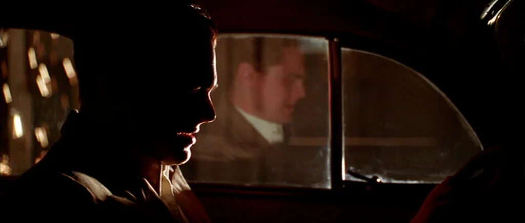 The Aviator (2004) movie still: medium — A dark car interior at night with limited ambient light from outside. A driver operates the steering wheel…