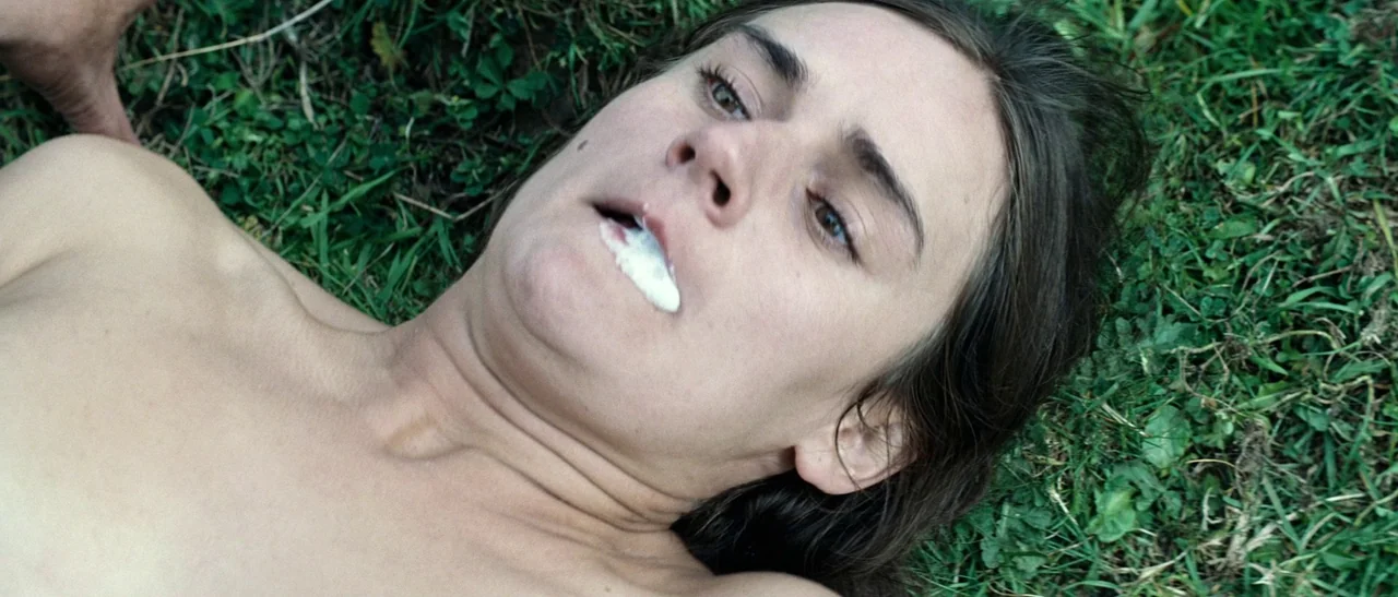 Outside Satan (2011) movie still: closeup — A person lies directly on a patch of green grass in an outdoor space. White foam gathers at the corner…