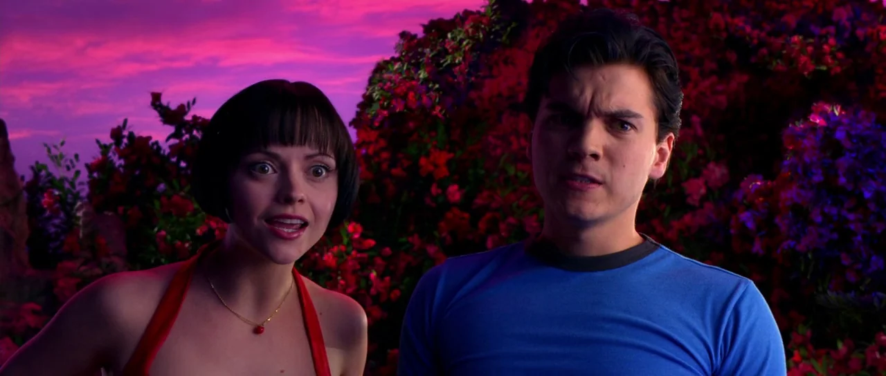 Speed Racer (2008) movie still: medium — A man and woman stand in front of dense, vibrant pink and red flowering bushes. A brilliant magenta…