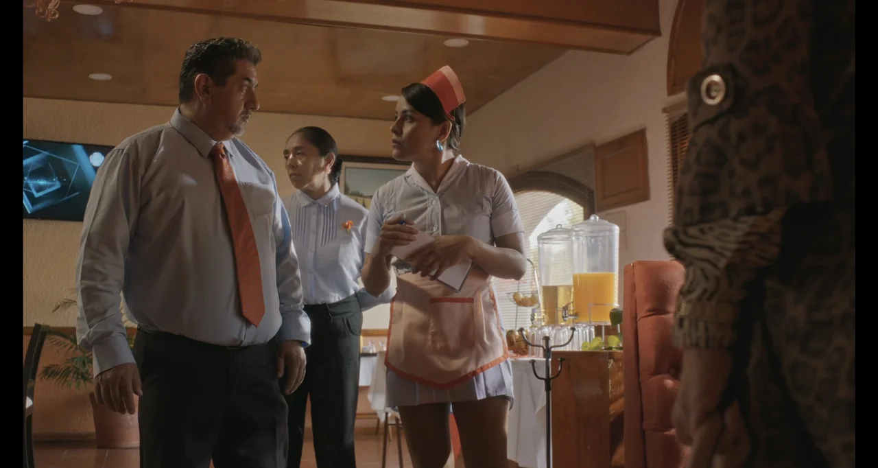 National Family (2023) movie still: medium — A well-lit restaurant dining room with wood paneling and a self-service juice station. A waitress…