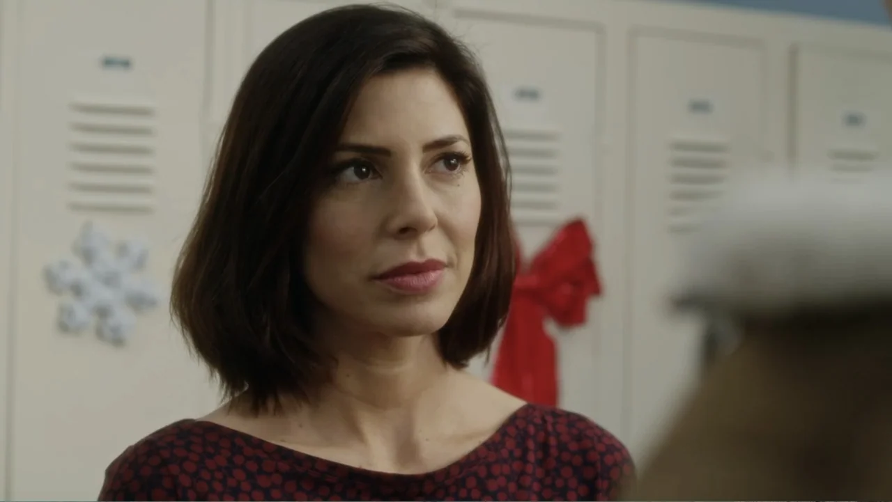 A Christmas Break (2020) movie still: closeup — A row of beige metal lockers with Christmas decorations lines a bright corridor. A woman stands in…