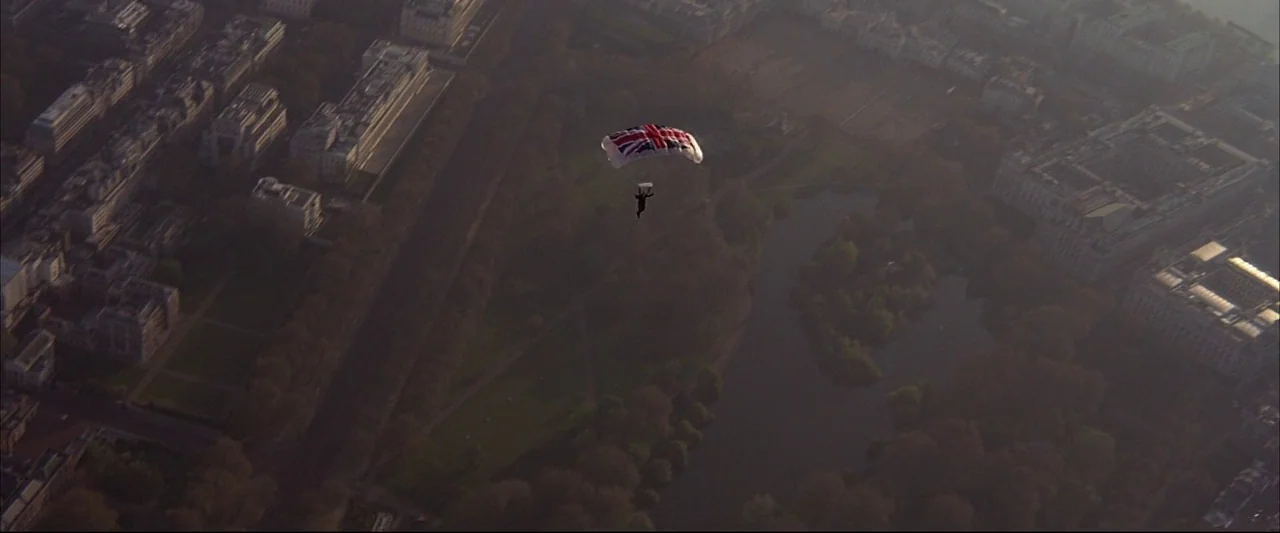 Die Another Day (2002) movie still: wide — A high-altitude view of a public park surrounded by city buildings and dense trees. A lone parachutist…