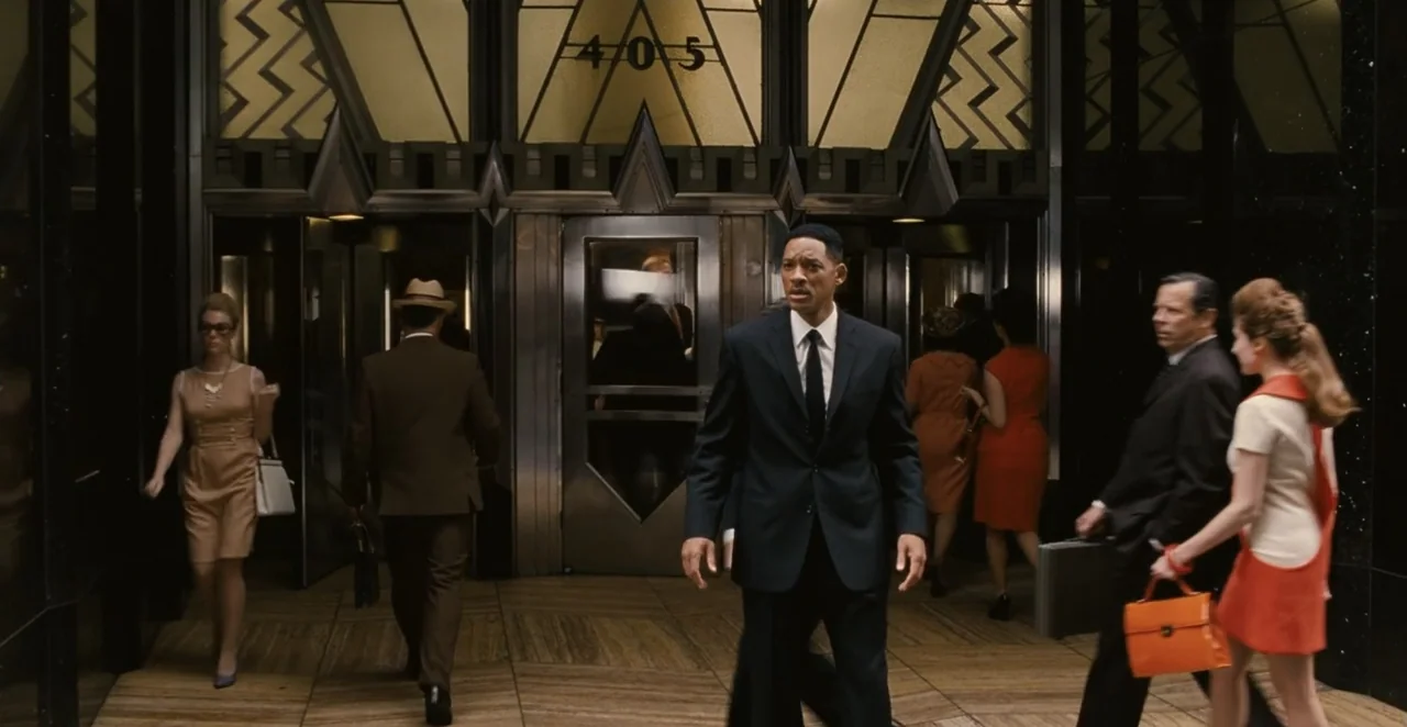 Men in Black 3 (2012) movie still: fullbody — An Art Deco building entrance features metal trim and stylized geometry above glass revolving doors. A…
