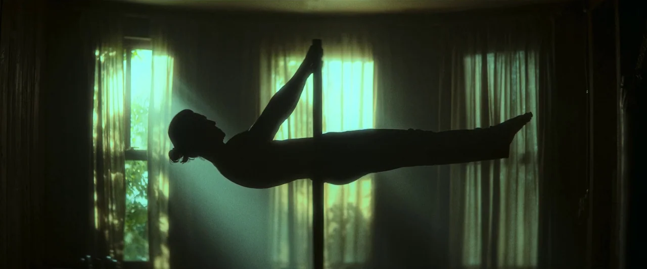 Ballerina (2023) movie still: fullbody — A silhouette of an athletic person is framed against bright light filtering through curtains. The subject…