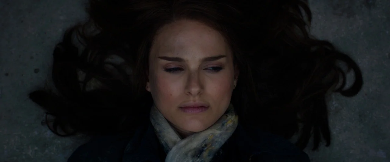 Thor: The Dark World (2013) movie still: closeup — A woman lies on a dark, textured concrete surface in dim light. She looks toward the side while…