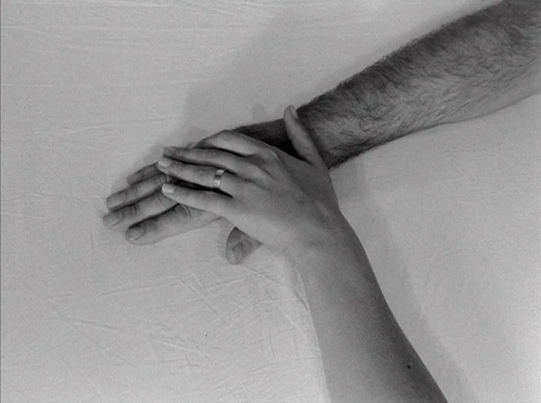 Une Femme Mariée (1964) movie still: closeup — A close-up view shows two hands resting on a plain white fabric surface. One hand with a silver band…