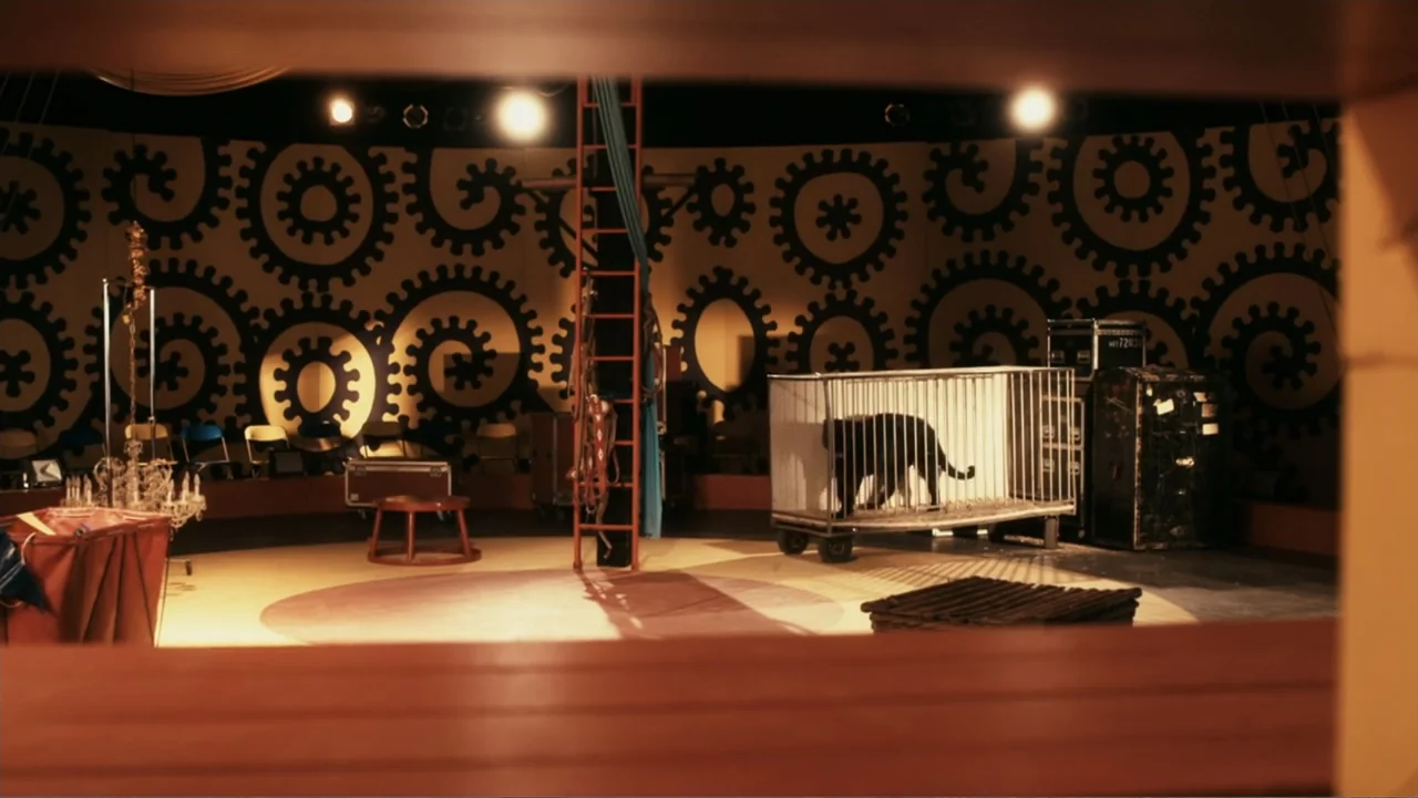 Sophie & Sheba (2010) movie still: wide — A circus tent interior features a patterned gear-themed backdrop and a central performance ring. A black…
