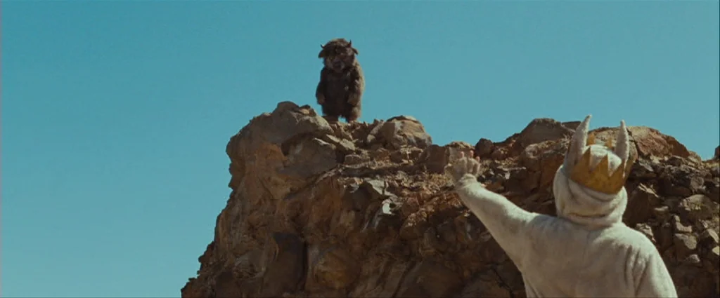 Where The Wild Things Are (2009) movie still: wide — A desolate rocky outcrop sits beneath a vast clear blue sky. A child in a wolf costume stands…