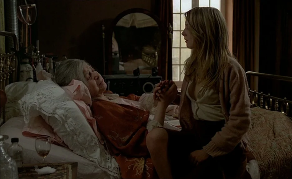 Black Moon (1975) movie still: medium — A dimly lit room with medical equipment and a wooden mirror in the background. A young woman sits on the…