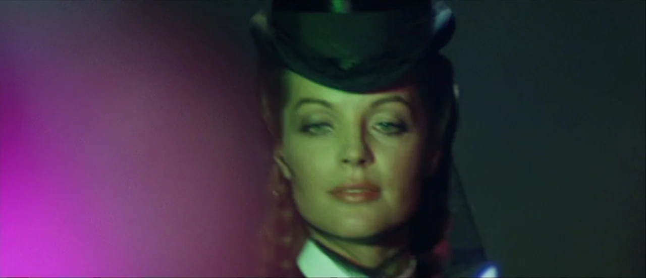 Ludwig (1973) movie still: closeup — A dark background with intense magenta and green stage lighting illuminates a woman's face. The subject wears a…