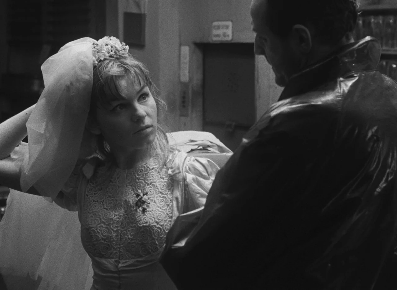 Pearls of the Deep (1965) movie still: medium — An interior space with a plain wall and an elevator door in the background. A woman in a wedding…