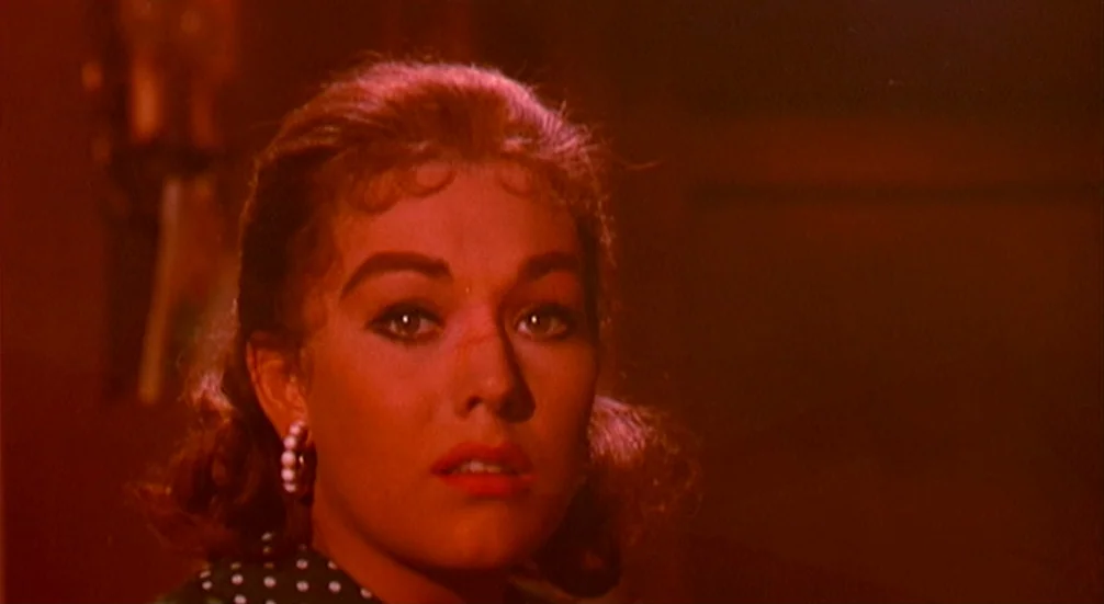 Vertigo (1958) movie still: closeup — A dimly lit interior space with an indistinct dark background. A young woman stares forward while lit by a…