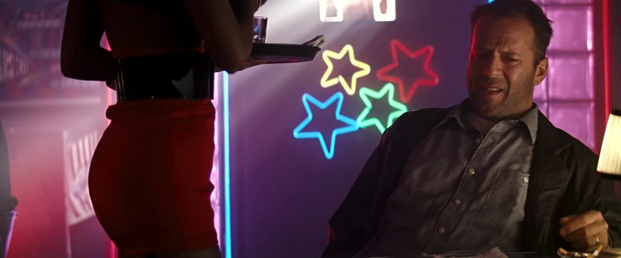 The Last Boy Scout (1991) movie still: medium — A dark bar interior features neon star-shaped lights mounted on a wall. A man sits at a table while…