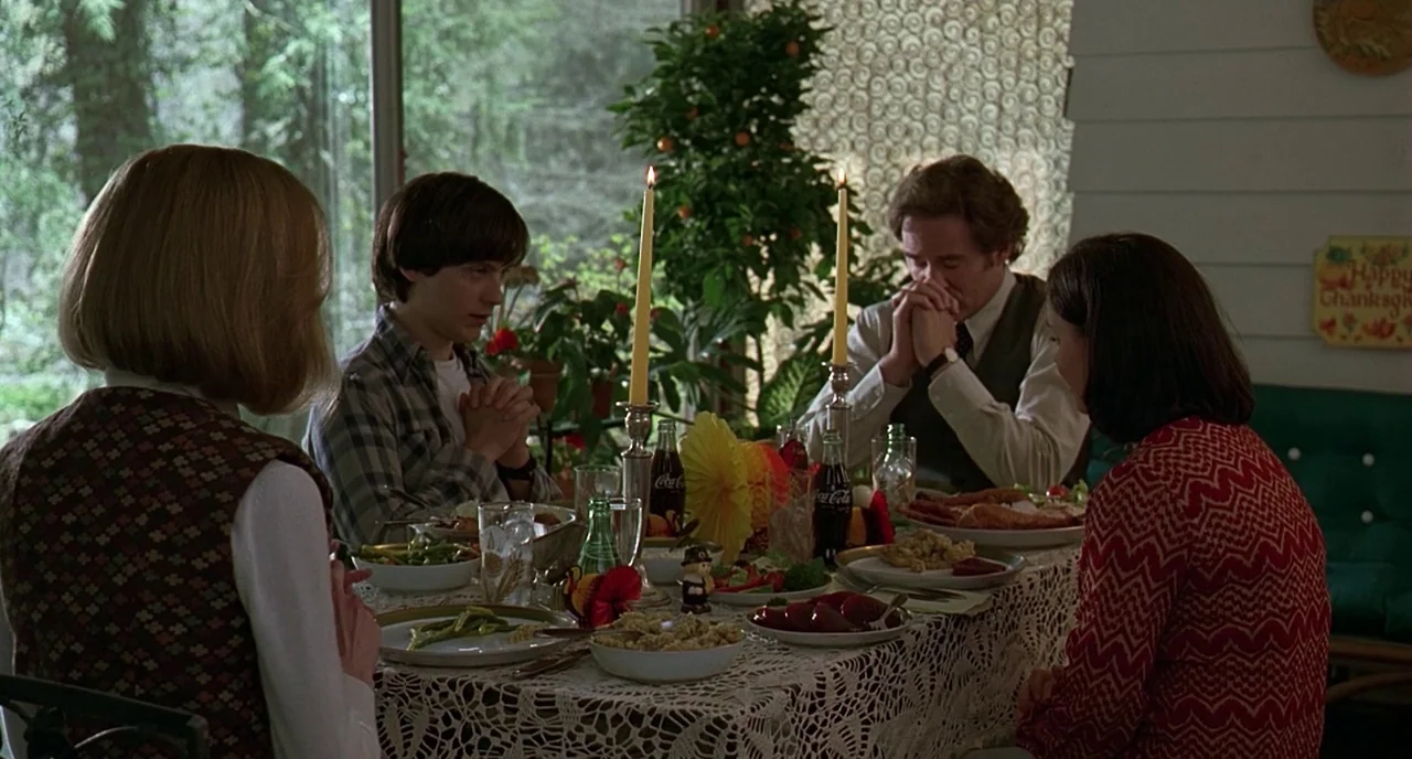 The Ice Storm (1997) movie still: medium — A family sits around a table set with lace tablecloth and holiday meal food. They hold hands in prayer…