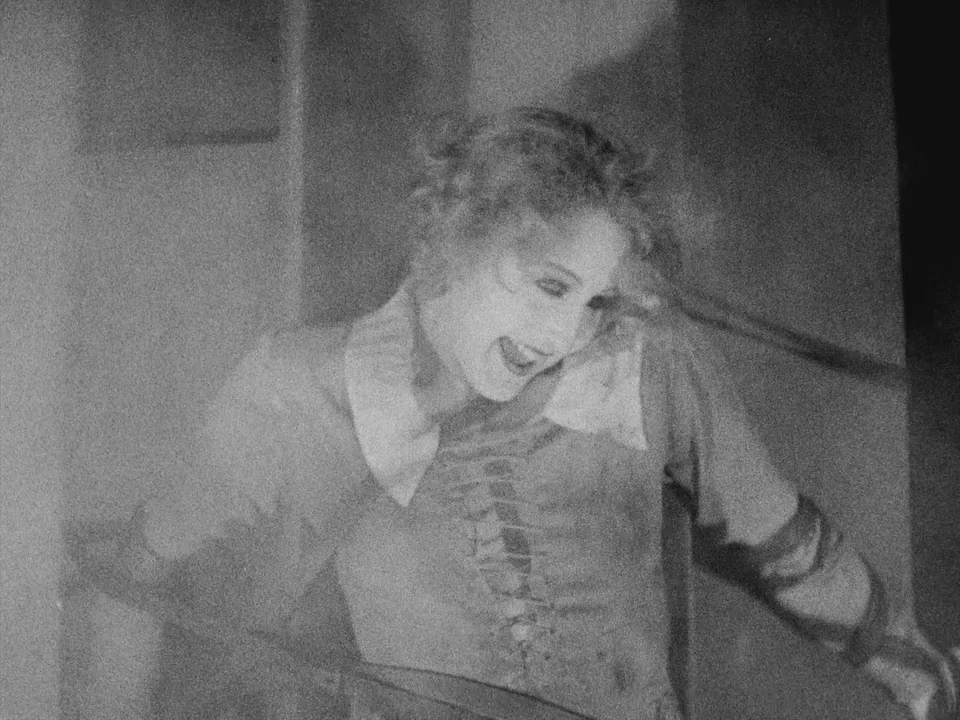 Metropolis (1927) movie still: medium — A dimly lit interior space with an indistinct dark background. A young woman leans forward while smiling,…
