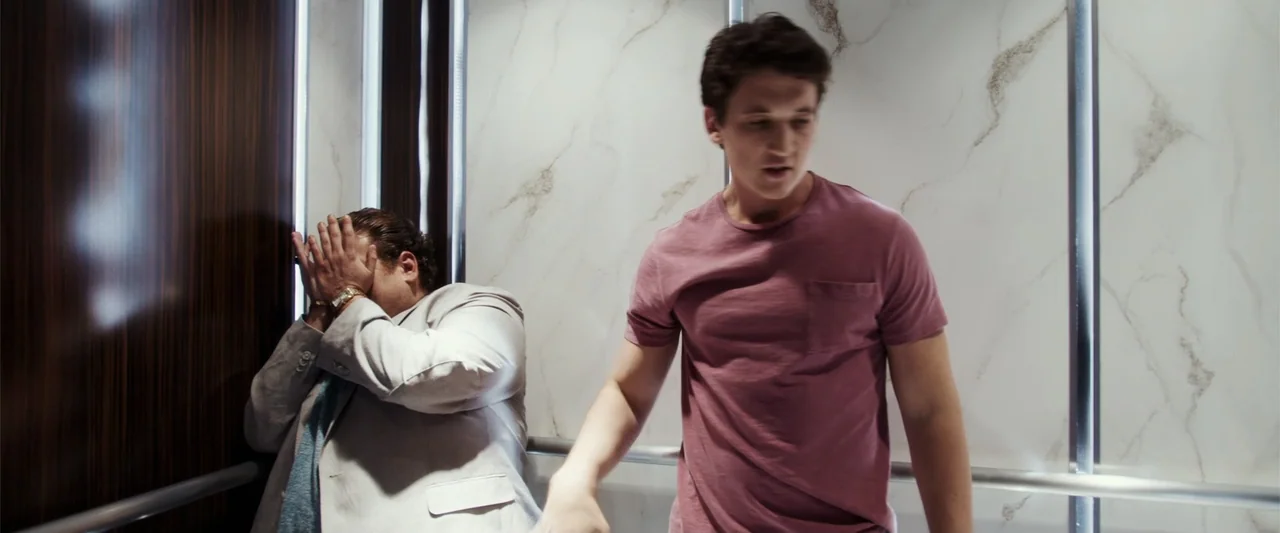 War Dogs (2016) movie still: medium — Modern elevator interior with white marble-patterned walls and dark wood accents. A man in a pink t-shirt…