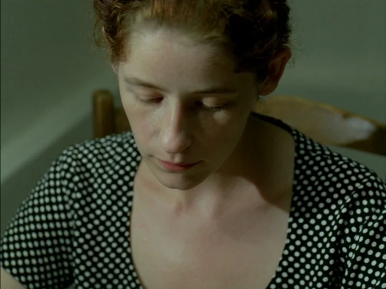 Helas Pour Moi (1993) movie still: closeup — A close-up of a woman in a room with neutral walls. The woman looks down with her eyes closed.
