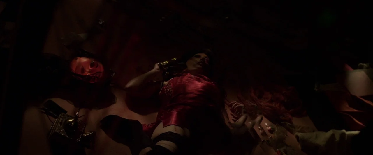 American Mary (2012) movie still: medium — A dimly lit space features a person lying on a flat surface among scattered items. The subject wears a…