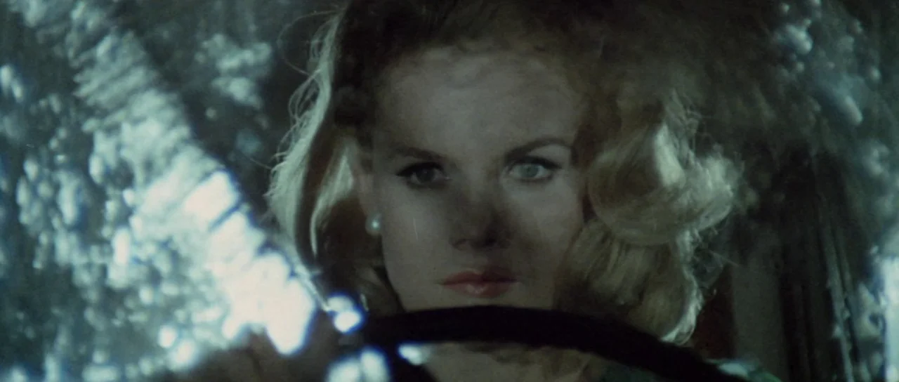 Orgasmo (1969) movie still: closeup — The interior of a vehicle features a rain-covered windshield obscuring the view. A woman with blonde hair sits…
