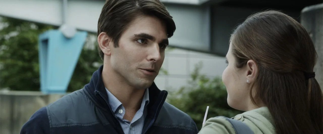 Final Destination 5 (2011) movie still: medium — Two individuals stand facing each other in an outdoor urban area with gray architecture. The man…