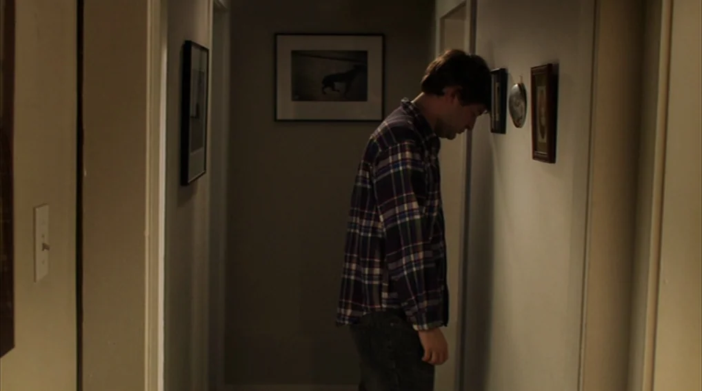 Your Sister’s Sister (2011) movie still: medium — A narrow residential hallway is lined with framed photographs on both off-white walls. A man…