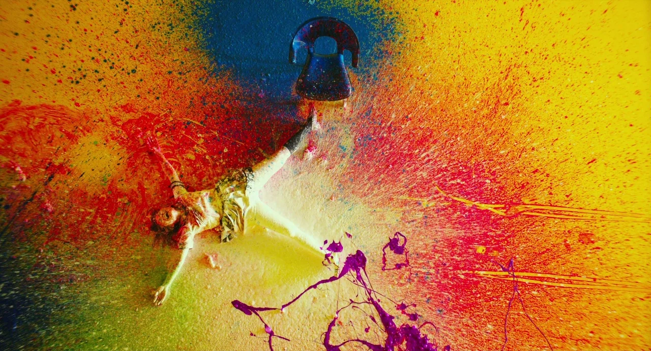 Making of: Antiporno (2016) movie still: wide — A studio floor covered in vibrant splashes of yellow, red, blue, and purple paint. A woman in a…