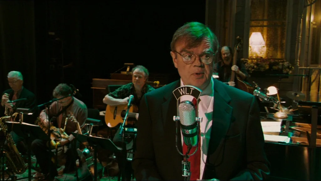 A Prairie Home Companion movie still: medium — A dimly lit recording studio features a musician ensemble playing instruments behind a radio…