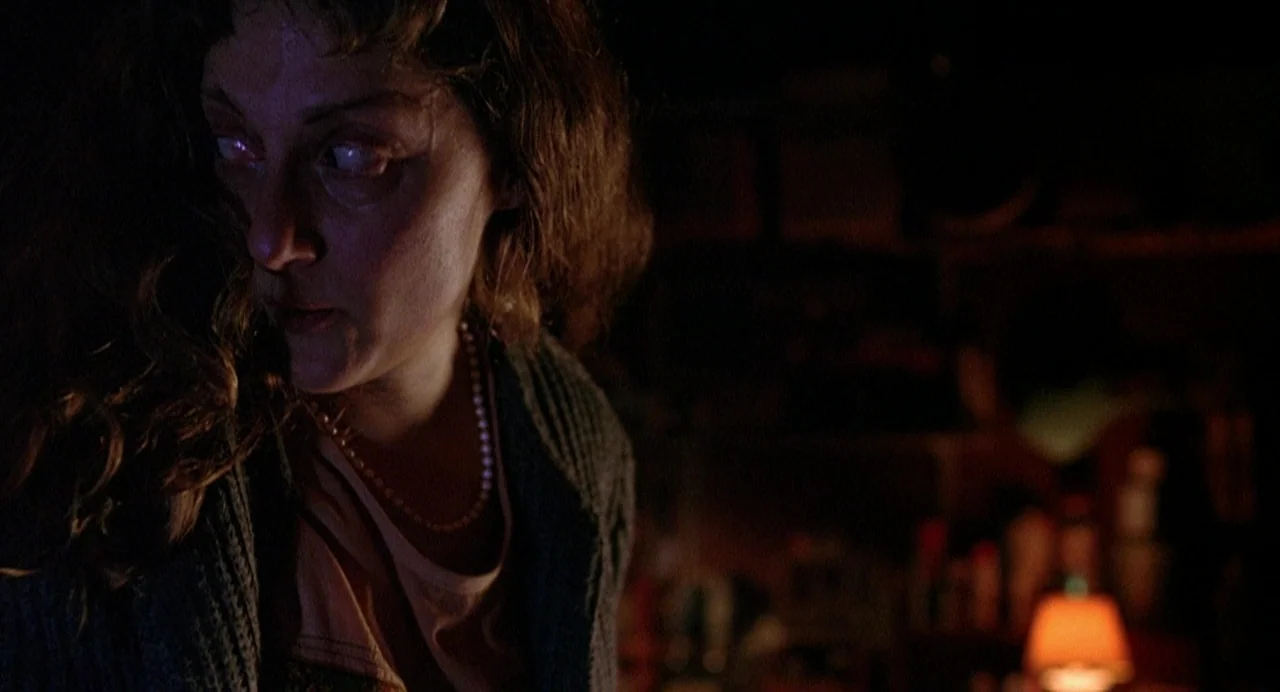 Office Killer (1997) movie still: closeup — A dimly lit interior space features a woman looking intently toward the edge of frame. The room is dark…
