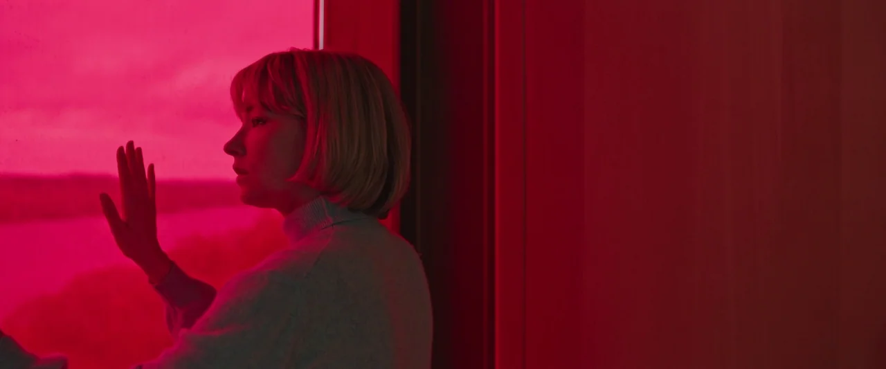 Swallow (2020) movie still: medium — A woman stands in a room illuminated entirely by intense magenta colored light. She faces a glass window with…