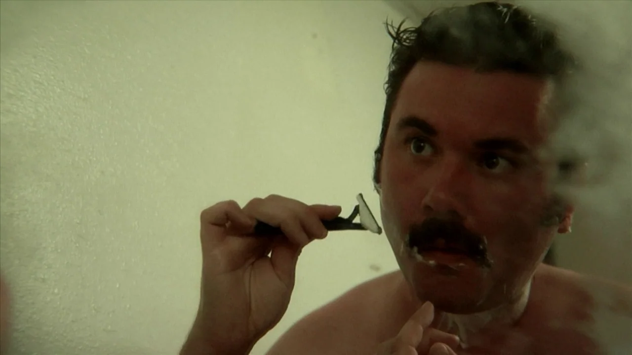 A Horrible Way To Die (2010) movie still: closeup — A man looks into a mirror in a dimly lit, nondescript bathroom. He uses a hand-held razor to…