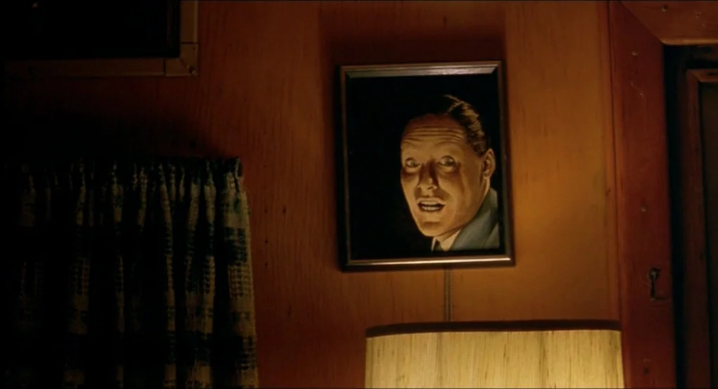 My Own Private Idaho (1991) movie still: closeup — A framed portrait of a man hangs on a wood-paneled wall at night. The man in the picture gazes…