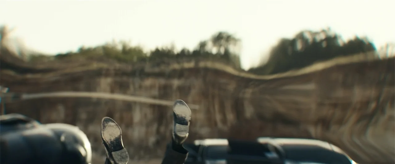 Hypnotic (2023) movie still: medium — An exterior rock quarry with stratified cliff walls forms the backdrop of the shot. A pair of worn leather…